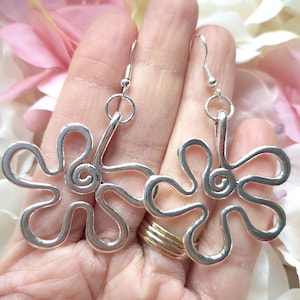 May include: A pair of silver flower-shaped dangle earrings with a spiral detail. The earrings have a simple, elegant design.