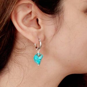 May include: A silver hoop earring with a turquoise stone pendant. The stone is a light blue color with brown veins.