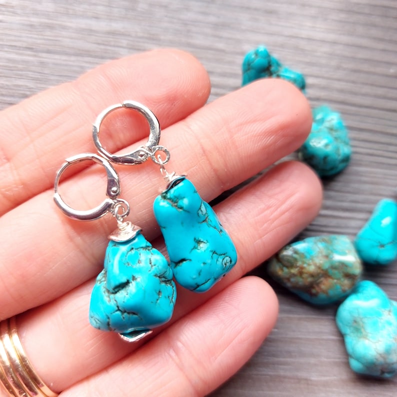 May include: A pair of silver hoop earrings with turquoise gemstone drops. The turquoise is a vibrant blue color with brown veins.