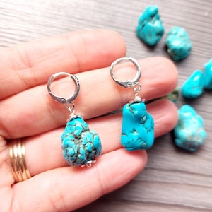 May include: A pair of silver hoop earrings with turquoise stones. The stones are a light blue color and have a rough, natural texture.