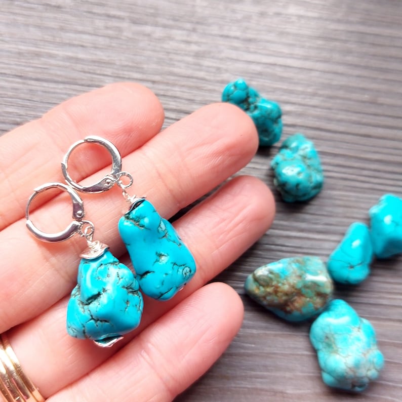 May include: Turquoise gemstone earrings with silver hoops. The turquoise stones are a vibrant blue color and have a natural, irregular shape.