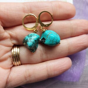 May include: Gold hoop earrings with turquoise gemstone drops. The turquoise is a vibrant blue-green color with brown veins.