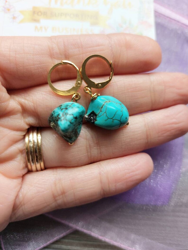 May include: Gold hoop earrings with turquoise gemstone drops. The turquoise is a vibrant blue-green color with brown veins.