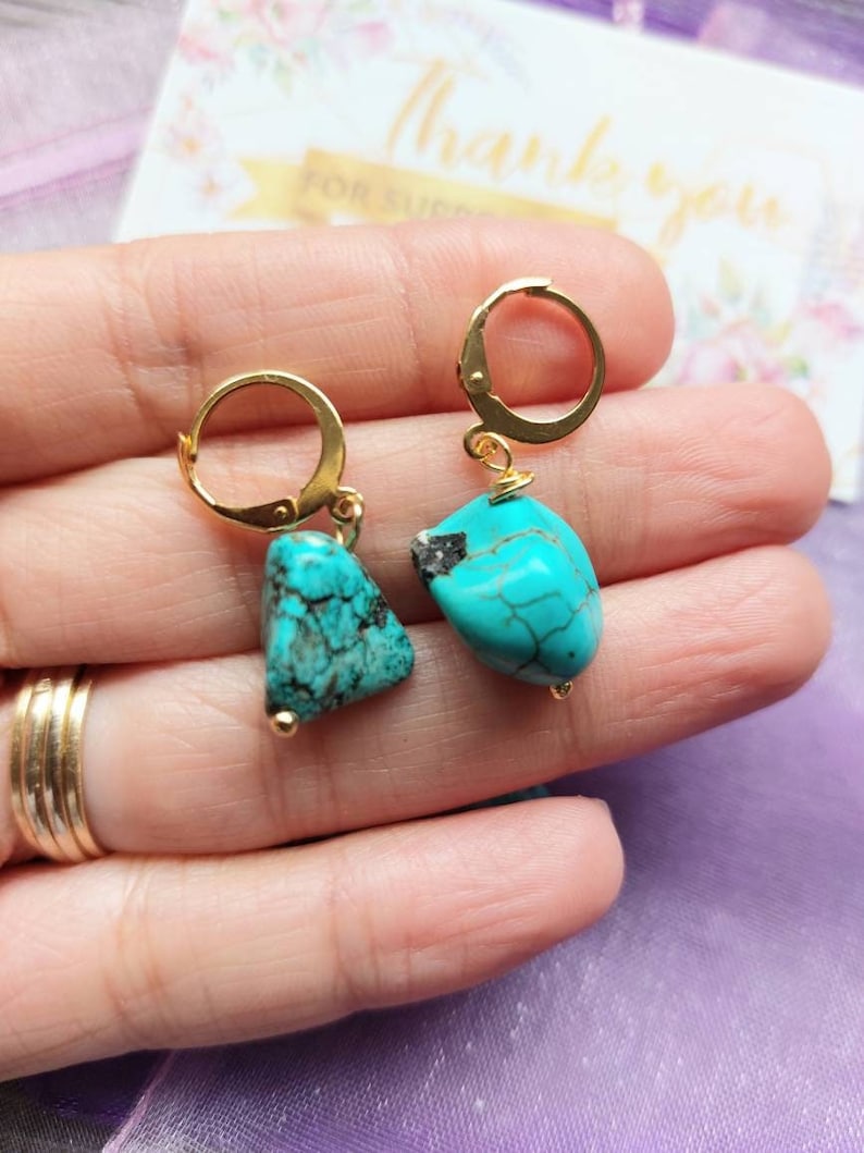 May include: A pair of gold hoop earrings with turquoise gemstone drops. The turquoise stones are a mottled blue-green color.