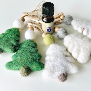 Peut inclure: Assortiment de décorations de Noël faites à la main et d'huile essentielle. Les ornements comprennent des sapins de Noël en feutre vert, des moutons en feutre blanc et des boules en feutre blanc. Une bouteille d'huile essentielle de lavande est également présente.