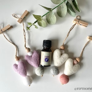 Könnte beinhalten: Vier Filz-Herz-Lufterfrischer mit Holzperlen und Schnur, die an Holz-Wäscheklammern hängen. Eine kleine Flasche Lavendel-Ätherisches Öl befindet sich in der Mitte.