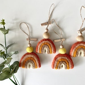 May include: Four felt rainbow ornaments with a wooden bead and a wooden clothespin. Each rainbow is made of five layers of felt in shades of orange, yellow, and brown.