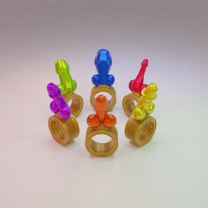 May include: Six colorful rings with a phallic shape on top. The rings are gold and the shapes are purple, green, blue, red, yellow, and orange.