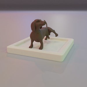 May include: A brown dachshund figurine standing on a white square base. The figurine is posed with its head turned to the side and its tail curled up.