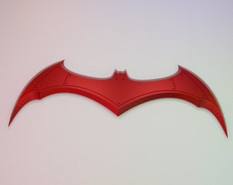 May include: A red bat-shaped logo with a pointed tip and a rounded body. The logo is mounted on a white wall.