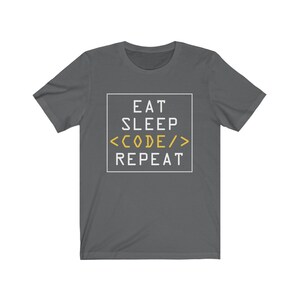 May include: A dark grey t-shirt with a white graphic that reads "Eat Sleep <CODE/> Repeat" in a box. The word "CODE" is in yellow.