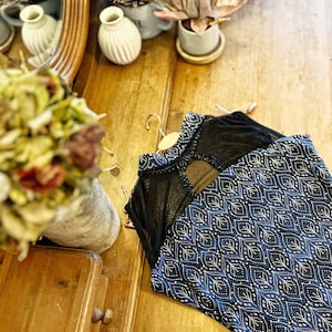 Può includere: Un top senza maniche blu e bianco con motivo e un pannello in rete nera sul retro. Il top è appeso su una superficie di legno.