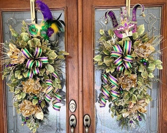 May include: Two Mardi Gras door wreaths with masks, feathers, and ribbons in green, purple, and gold. The wreaths are hanging on a wooden door with glass panels. The door has brass handles.