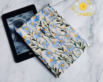 Pode incluir: Uma capa para leitor de e-books em tecido bege com flores bordadas azuis e amarelas. A capa tem um fecho de botão e o texto "Forever Unique Craft" é visível no fundo.