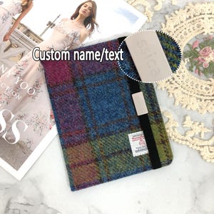 Pode incluir: Um porta-passaporte xadrez azul, verde, rosa e roxo com fecho de elástico preto. O porta-passaporte tem um pequeno rótulo branco com o texto "Harris Tweed" e um rótulo branco com o texto "SICS".