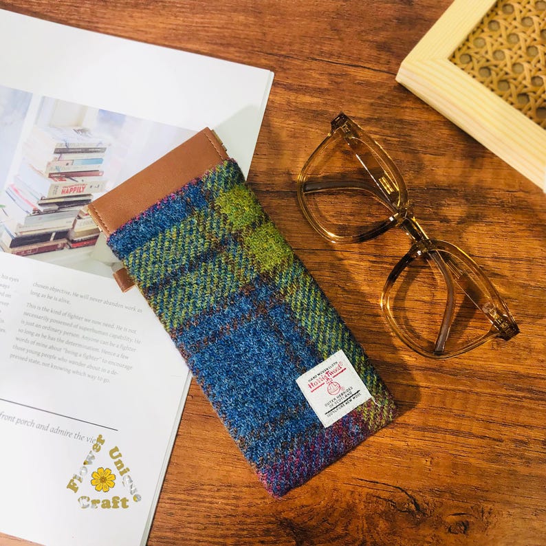 May include: A blue, green and brown plaid glasses case with a brown leather trim. The case has a small white label with the text "Harris Tweed" and "Hand Woven in the Outer Hebrides".