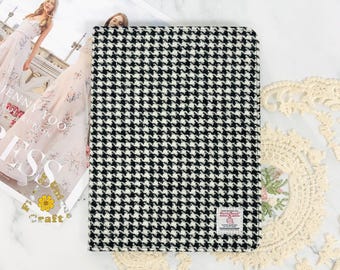 May include: Black and white houndstooth patterned notebook cover. The cover is made of a soft, textured fabric. The notebook cover has a small red label with the text "Harris Tweed" on it.