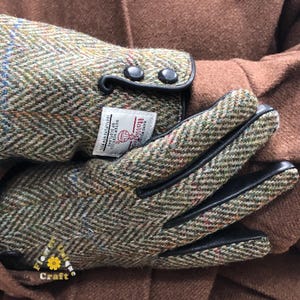 Op de afbeelding: Groen en bruin tweed handschoenen met zwarte leren afwerking en knopen. De handschoenen hebben een label met de tekst "Harri The Hand and Glove Craft Outer Hebrides of Scotland 100% Pure New Wool"
