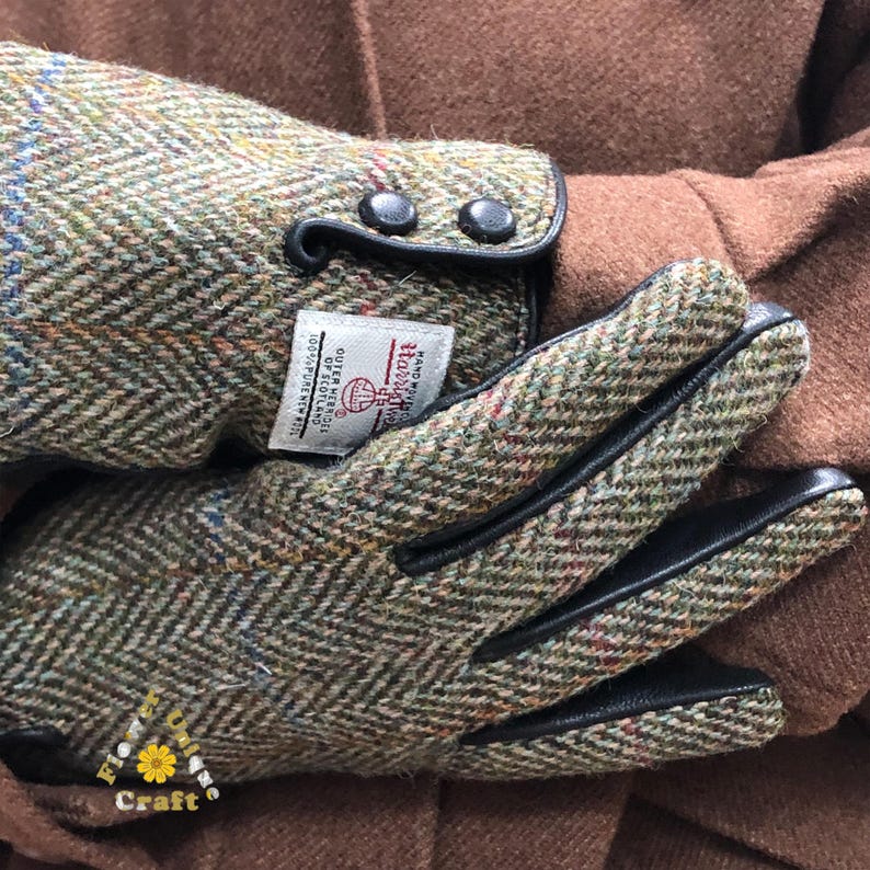 Op de afbeelding: Groen en bruin tweed handschoenen met zwarte leren afwerking en knopen. De handschoenen hebben een label met de tekst "Harri The Hand and Glove Craft Outer Hebrides of Scotland 100% Pure New Wool"