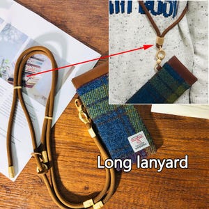 May include: A long, brown lanyard with gold-colored metal accents and a matching case. The case is made of blue and green plaid fabric with a brown leather top. The text "Long lanyard" is visible.