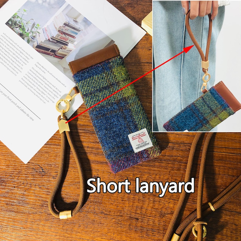 May include: A blue, green, and brown plaid phone case with a brown leather top and a short lanyard. The lanyard is a tan color with gold-colored metal accents. The case has a small white tag with red text.