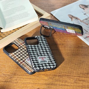 May include: A collection of phone cases with various tweed patterns. One case features a colorful, speckled design, while others display classic houndstooth patterns in black and white, and brown and beige. Each case has a black frame and a metal ring.