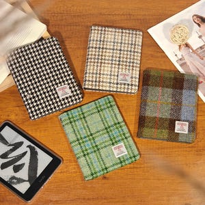 May include: Four patterned book covers in black and white houndstooth, brown and tan, green plaid, and brown plaid. Each cover has a small white tag. A Kindle e-reader is visible in the lower left corner.