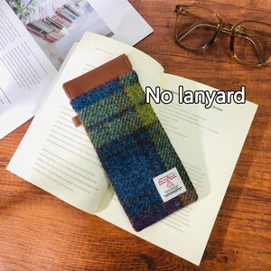 May include: A brown leather and tweed glasses case with a red and white label that says "Harris Tweed" and "Hand Woven." The case is lying on a white page with the text "No lanyard" written on it.