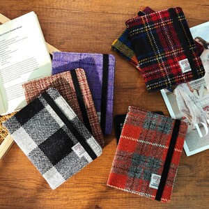 May include: A collection of colorful tweed tablet covers in various plaid patterns. The covers are in shades of red, black, gray, purple, and brown. Each cover has a black elastic band and a small label.