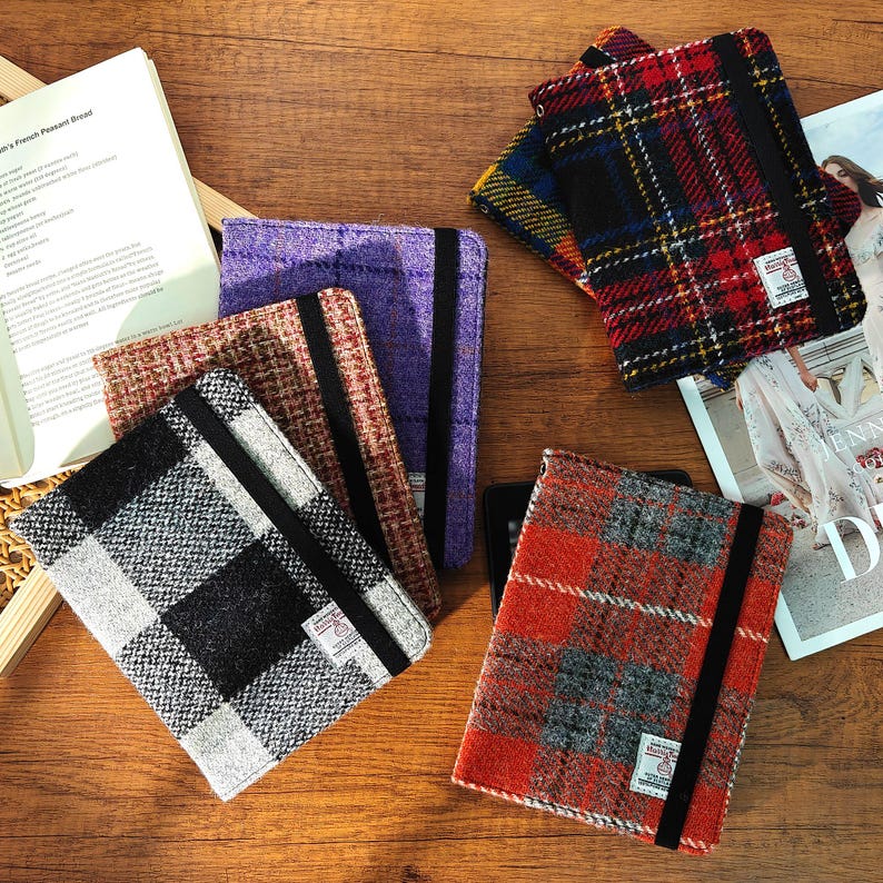 May include: A collection of colorful tweed tablet covers in various plaid patterns. The covers are in shades of red, black, gray, purple, and brown. Each cover has a black elastic band and a small label.