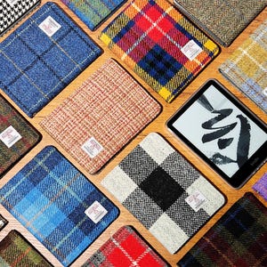 May include: A collection of wallets in various tweed and plaid patterns, alongside an e-reader. The wallets showcase designs in blue, red, and green. An e-reader with a black and white graphic is also present.