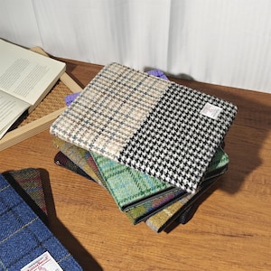 May include: A stack of colorful tweed fabric pouches. The top pouch is split between a black and white houndstooth pattern and a beige and brown plaid. Other pouches feature green, blue, and yellow plaid patterns. A book is open in the background.