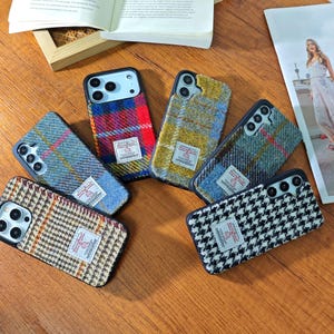 Puede incluir: Varias fundas para teléfonos móviles con diseños de tela de tweed, incluyendo cuadros y pata de gallo. Cada funda tiene una etiqueta de tela con texto. Las fundas son en tonos azules, rojos, amarillos y marrones.