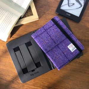 Op de afbeelding: Paarse geruite Kindle-hoes met een zwarte elastische band en een klein wit label. De hoes is open en toont een grijs interieur met bandjes en de tekst "My love". Een Kindle e-reader en een open boek zijn ook zichtbaar.