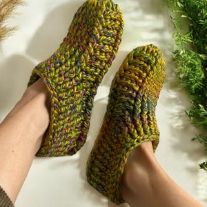 May include: A pair of green, yellow, and purple crocheted slippers. The slippers are made with a chunky yarn and have a simple, comfortable design.