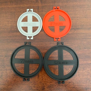 May include: Four round filter holders in different sizes. The holders are made of black, gray, and orange plastic. The sizes are 58mm, 67mm, 77mm, and 82mm.