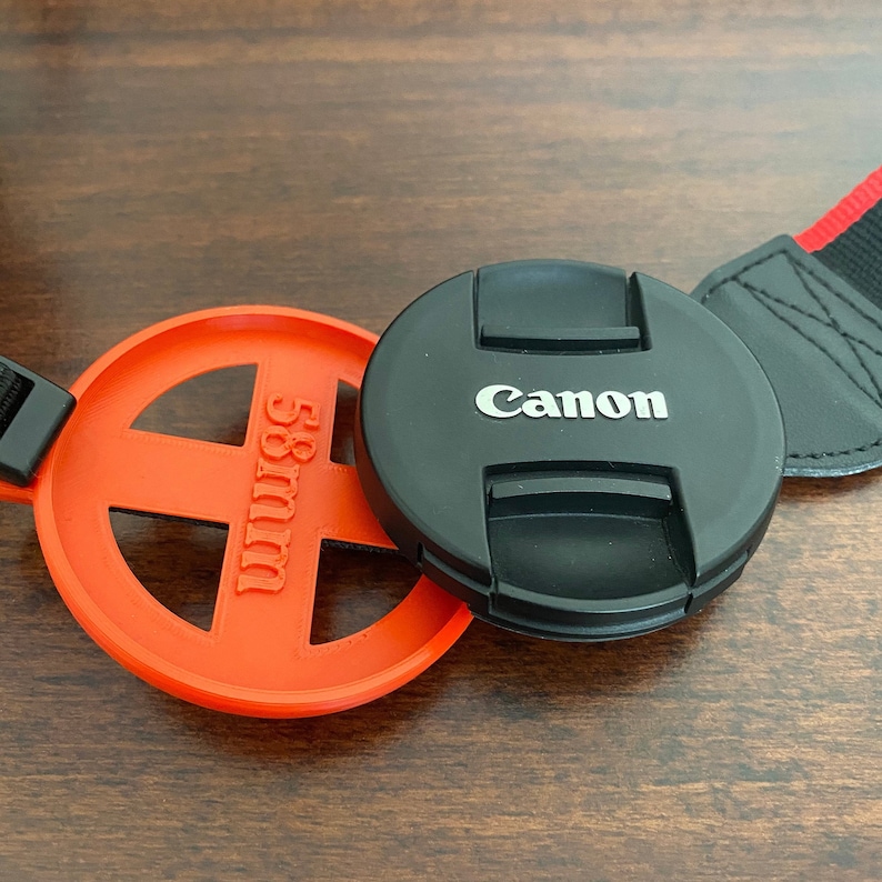 May include: A black Canon lens cap with a red 58mm lens cap holder.
