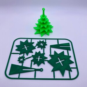 May include: A green plastic Christmas tree ornament with a star on top. The ornament is disassembled and laid out on a green plastic sheet with instructions for assembly.