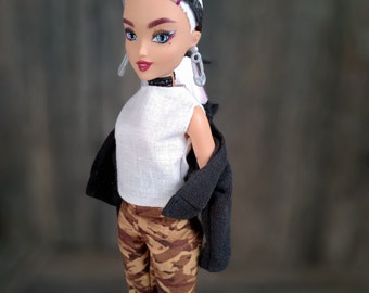 May include: A fashion doll with white hair and purple streaks, wearing a white tank top, black jacket, camouflage pants, black boots, and goggles.