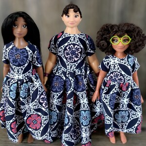 May include: Three dolls wearing blue and white patterned dresses. The dolls have brown hair and are wearing different hairstyles. The doll in the middle has a green headband.