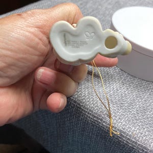 May include: White porcelain ornament of a girl with a butterfly on her dress. The ornament has a gold string and the words "Precious Moments" and "1978 Enesco" on the back.