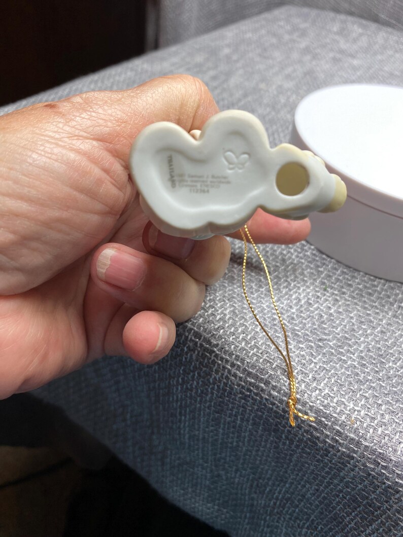May include: White porcelain ornament of a girl with a butterfly on her dress. The ornament has a gold string and the words "Precious Moments" and "1978 Enesco" on the back.