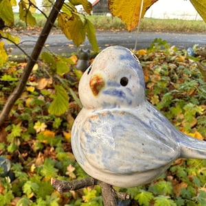 Könnte beinhalten: Eine blaue und weiße Keramik-Vogelfigur, die auf einem Ast sitzt. Der Vogel hat eine detaillierte, strukturierte Oberfläche und einen kleinen, braunen Schnabel.