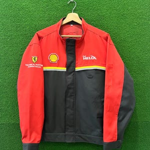 May include: A red and black jacket with the Shell logo and the text "Technical Partner Scuderia Ferrari" on the left side and the text "Shell Helix" on the right side.