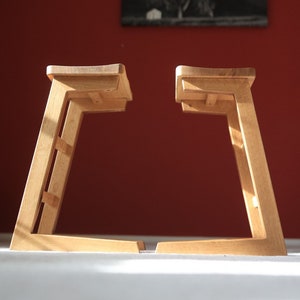 Peut inclure: Deux tabourets en bois au design simple et moderne. Les tabourets sont en bois clair et ont une forme rectangulaire. Ils sont tous les deux légèrement inclinés vers l'avant, ce qui leur donne un aspect dynamique.
