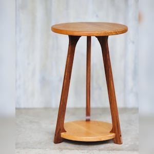 May include: A wooden side table with a round top and a lower shelf. The table has three legs that are angled inwards.