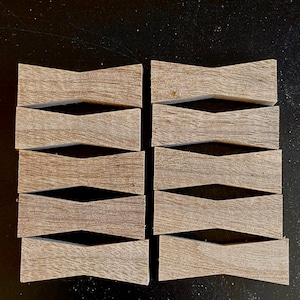 May include: Ten wooden, light brown, bow tie-shaped coasters with a wavy design. The coasters are arranged in two rows of five.