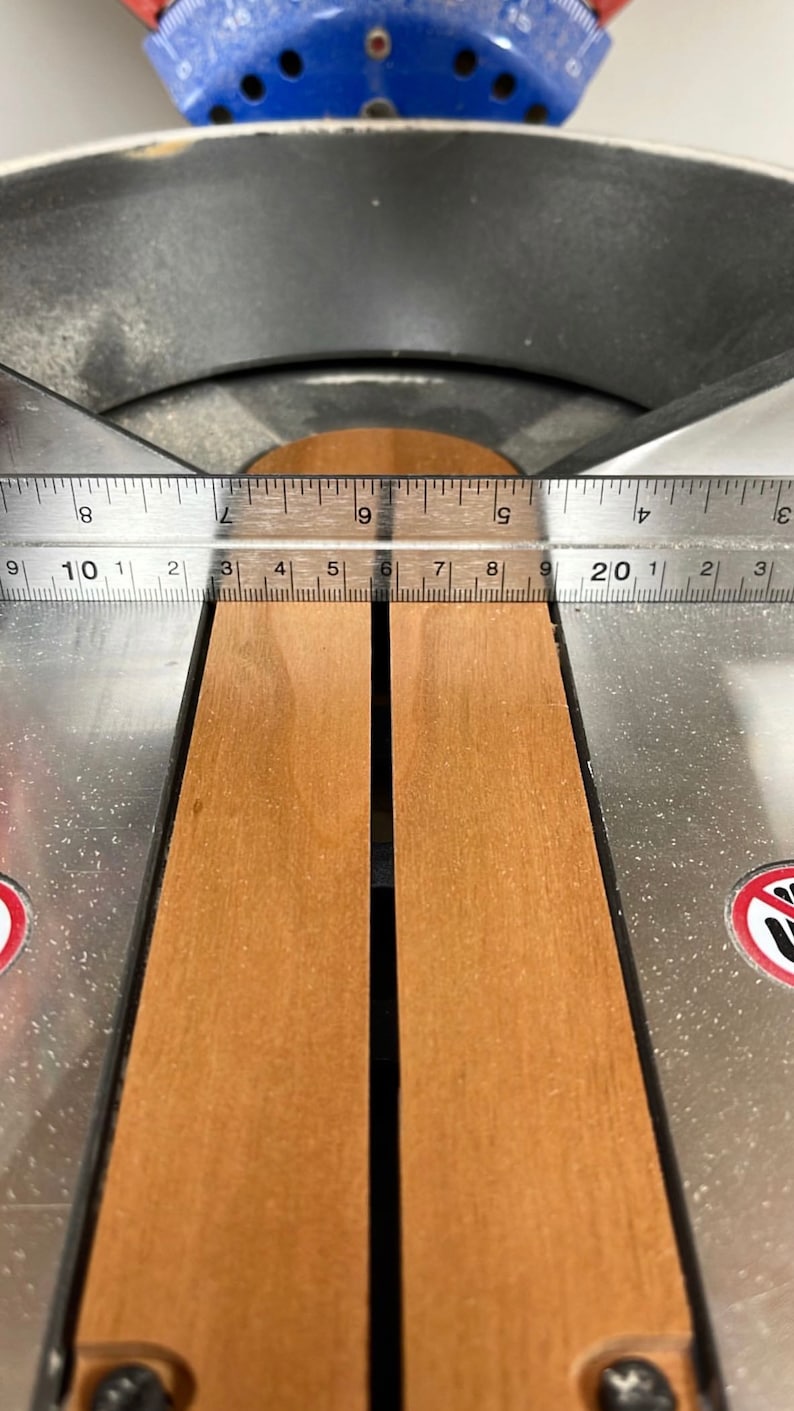 Puede incluir: Primer plano de una sierra de mesa de metal con dos tablas de madera en su lugar. Las tablas est&aacute;n alineadas con una regla que indica "9 10 1 2 3 4 5 6 7 8 9 20 1 2 3".