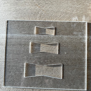 Op de afbeelding: Een transparant acrylplaat met drie verschillende maten uitgesneden vlinderdasvormen. De vormen zijn op elkaar gestapeld.