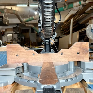 Peut inclure: Vue rapproch&eacute;e d'une scie &agrave; onglets avec une extension en bois fix&eacute;e &agrave; la base. La scie est install&eacute;e sur une table en bois et est pr&ecirc;te &agrave; couper.